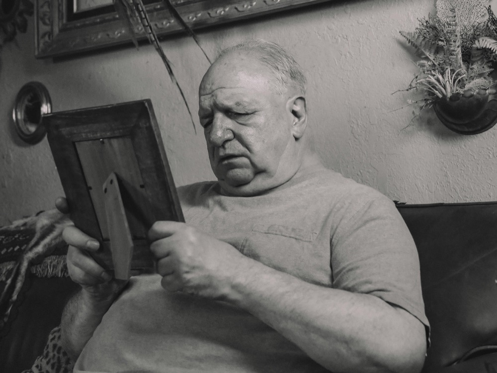 An older man on his sofa at home, looking at a framed photograph
