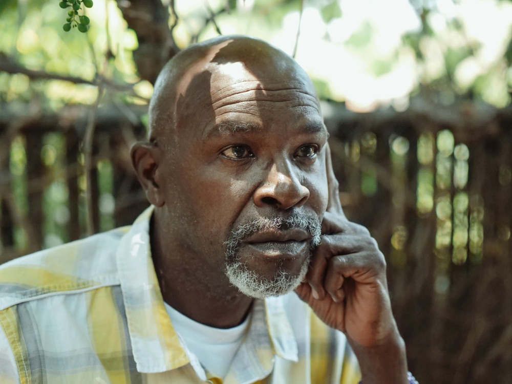 A man in a checked shirt, deep in thought, photographed outdoors in dappled light